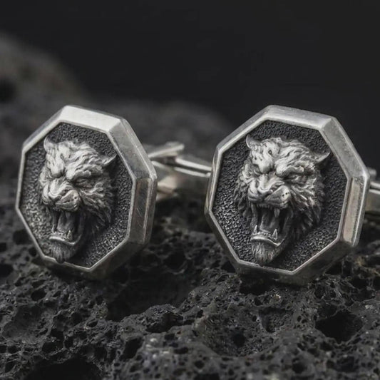 An oxidized tiger head cufflink pair rests on dark volcanic rock in a macro studio close-up, showing a fierce roaring big cat inside octagon frames.