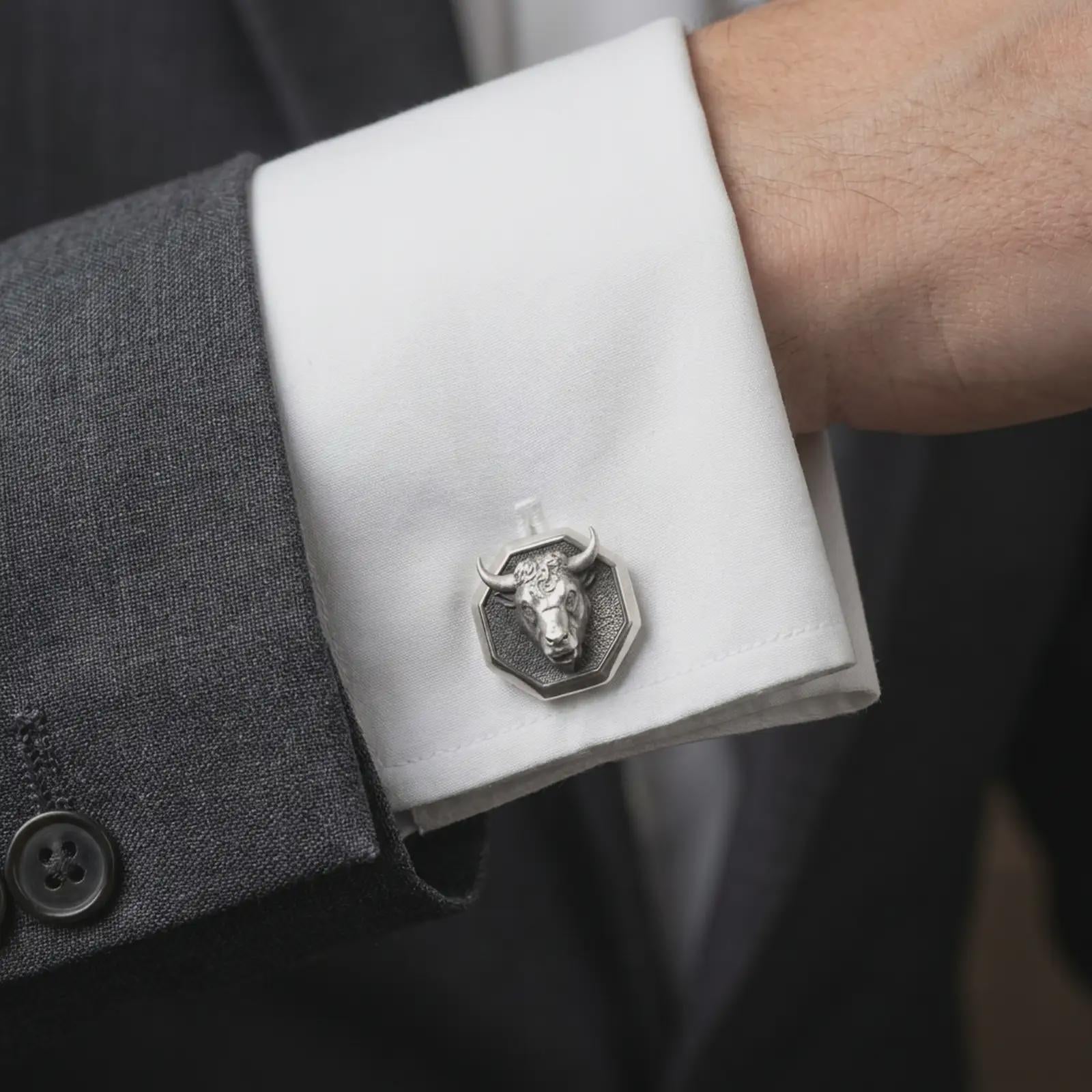 An oxidized bull head cufflink is worn on a white shirt cuff in a close-up lifestyle shot, styled with a dark suit for a bold masculine look.
