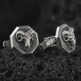 Load image into Gallery viewer, An oxidized ram head cufflink pair rests on dark volcanic rock in a macro studio close-up, showing sculpted curled horns and animal detail inside octagon frames.
