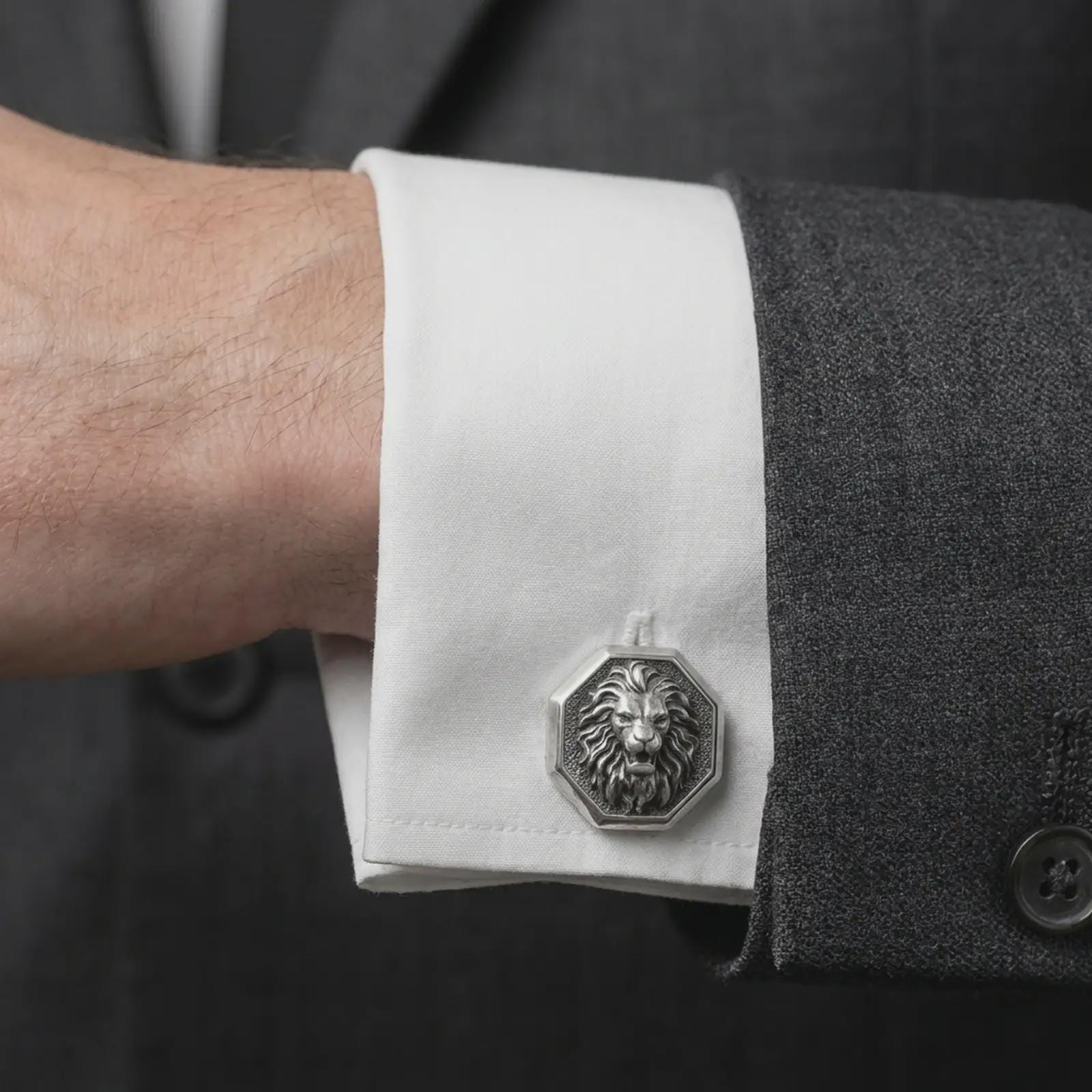 An oxidized lion head cufflink is worn on a white shirt cuff in a close-up lifestyle shot, styled with a dark suit for a bold formal look.