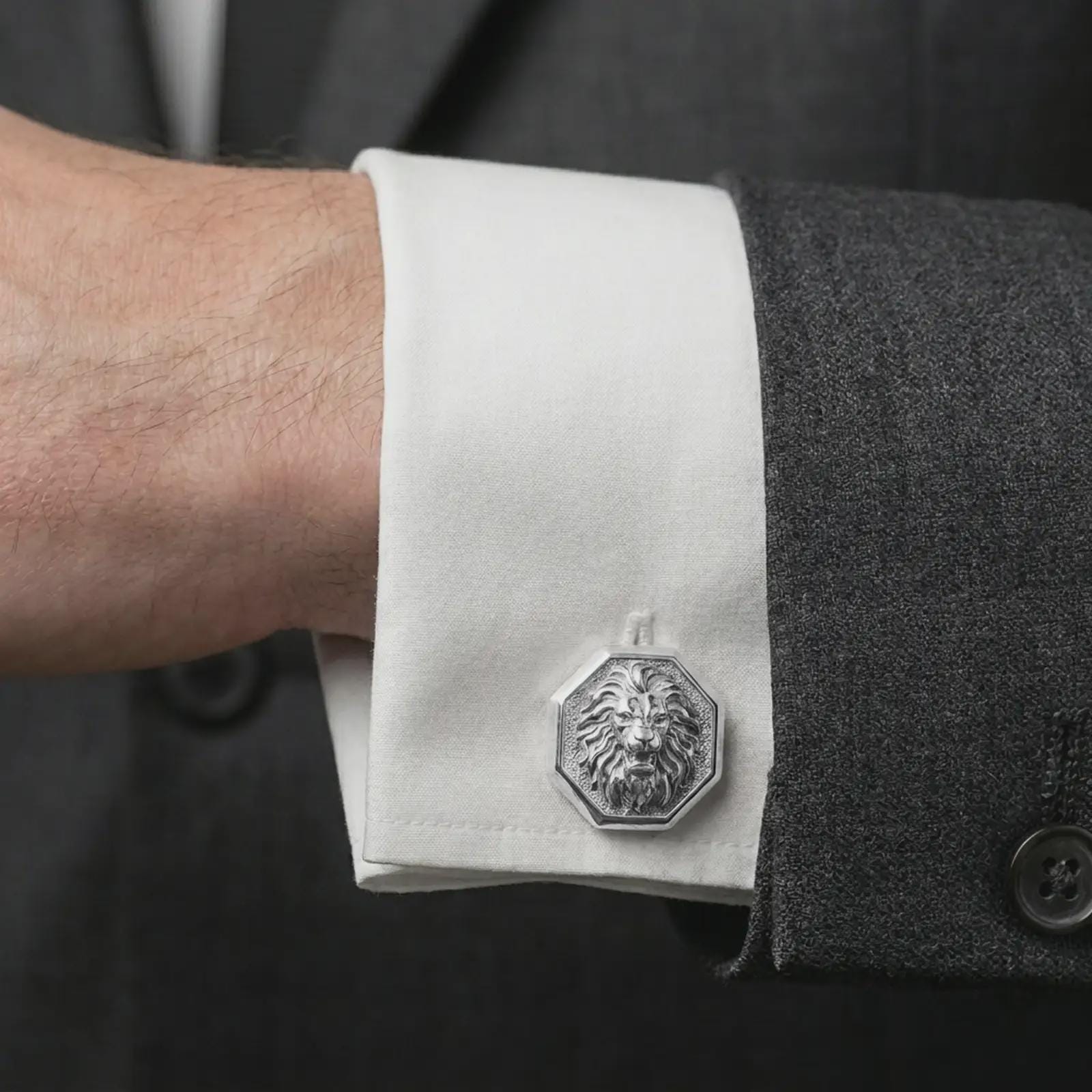 A polished silver lion head cufflink is worn on a shirt cuff in a premium close-up lifestyle image, showing the sculpted roaring lion face clearly.
