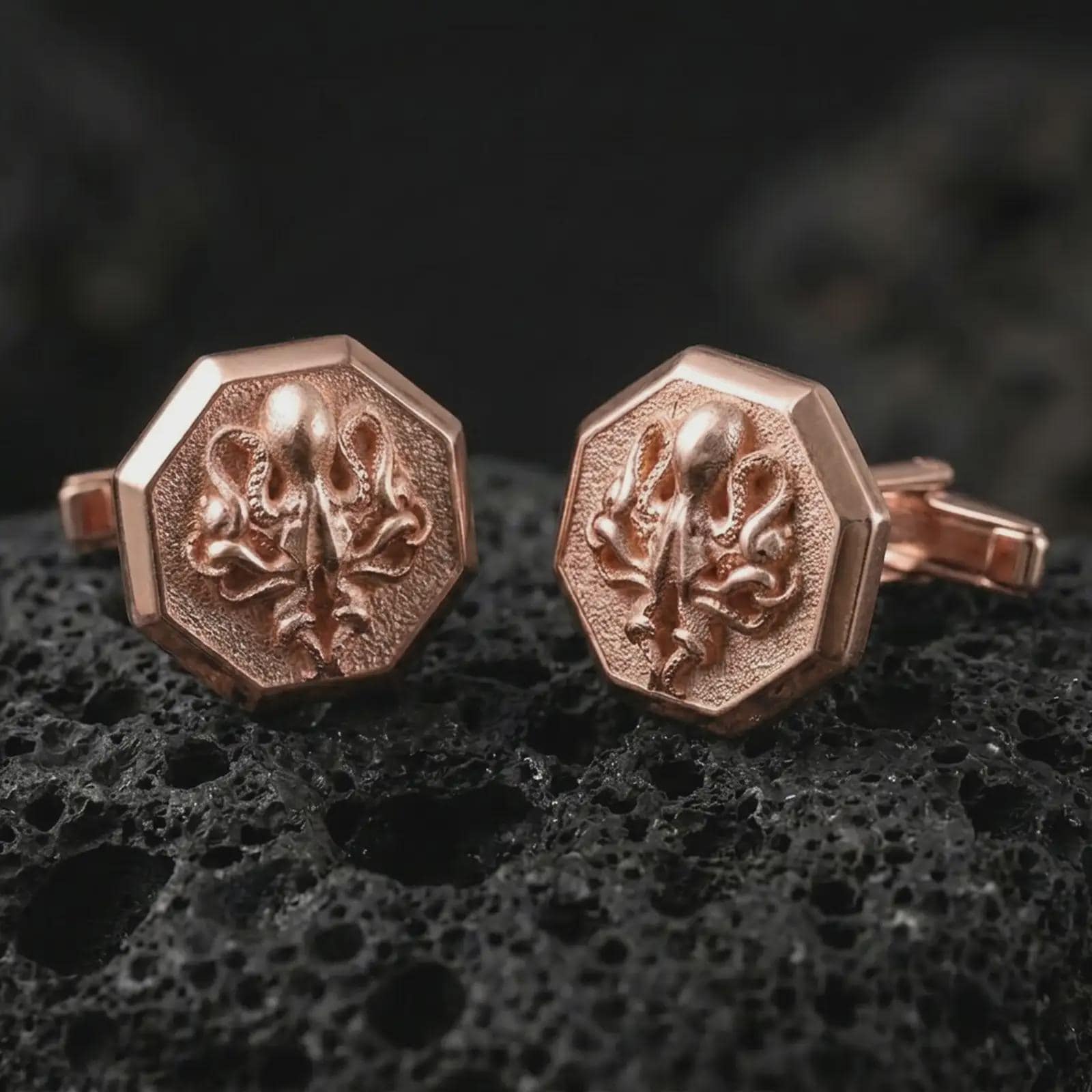 Rose gold plated octopus cufflinks are photographed on porous volcanic rock in a close-up studio composition with refined luxury lighting and detailed ocean-inspired features.