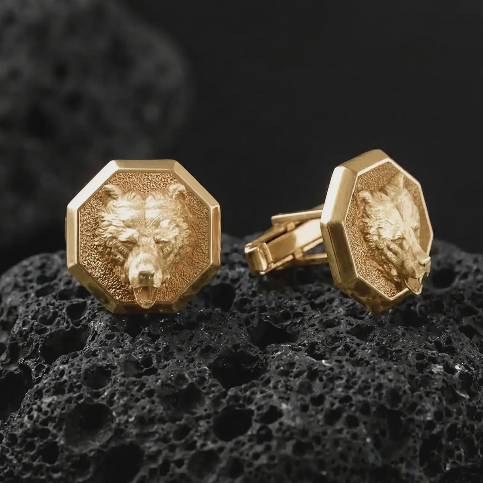 Gold plated bear head cufflinks sit on textured volcanic rock in a dramatic studio macro shot, highlighting the powerful wildlife motif and formal accessory design.