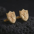 Load image into Gallery viewer, Gold plated Saint Michael cufflinks sit on textured volcanic rock in a dramatic studio macro shot, highlighting the Catholic archangel protection motif.

