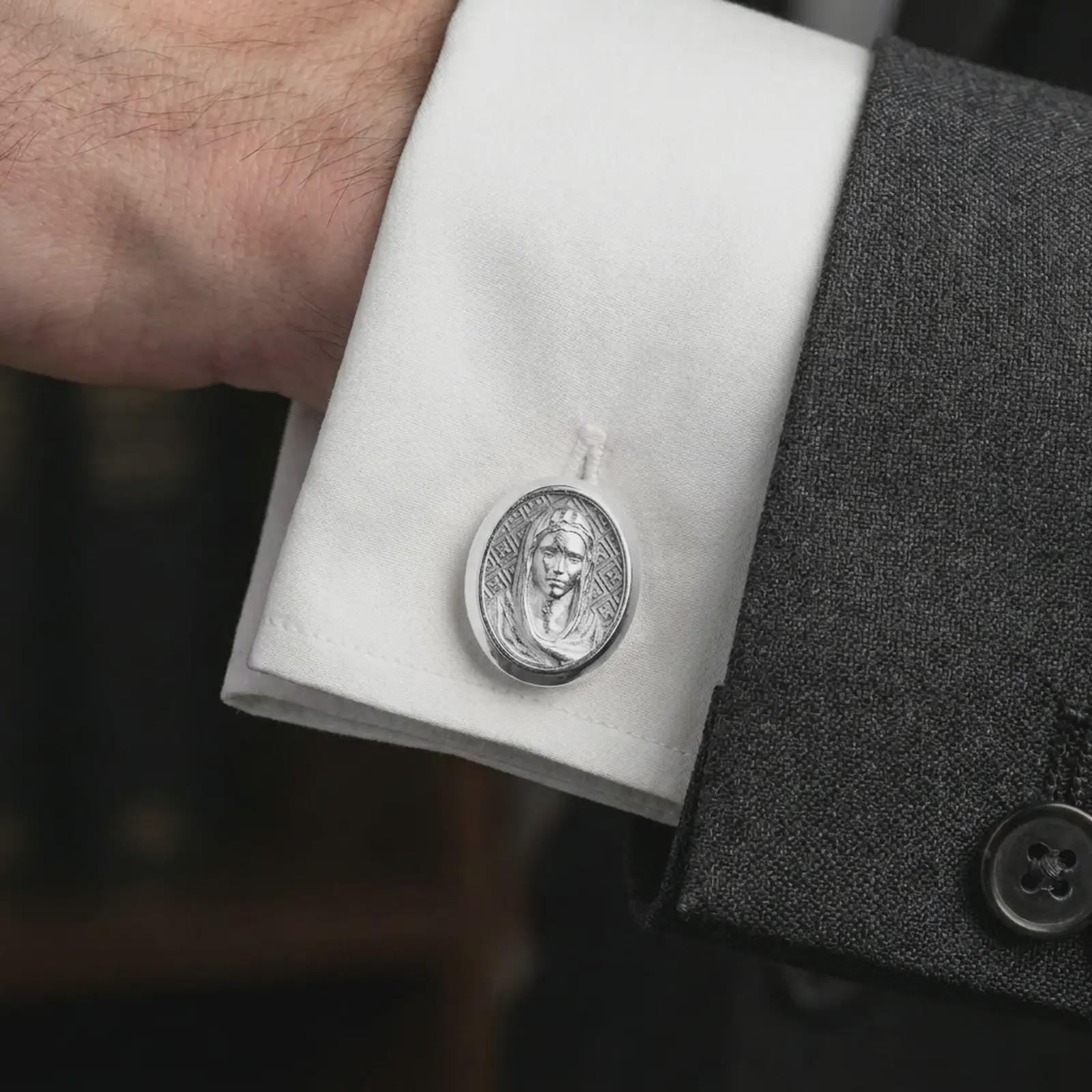 A polished silver Virgin Mary cufflink is worn on a shirt cuff in a premium close-up lifestyle image, showing the Marian portrait relief clearly.