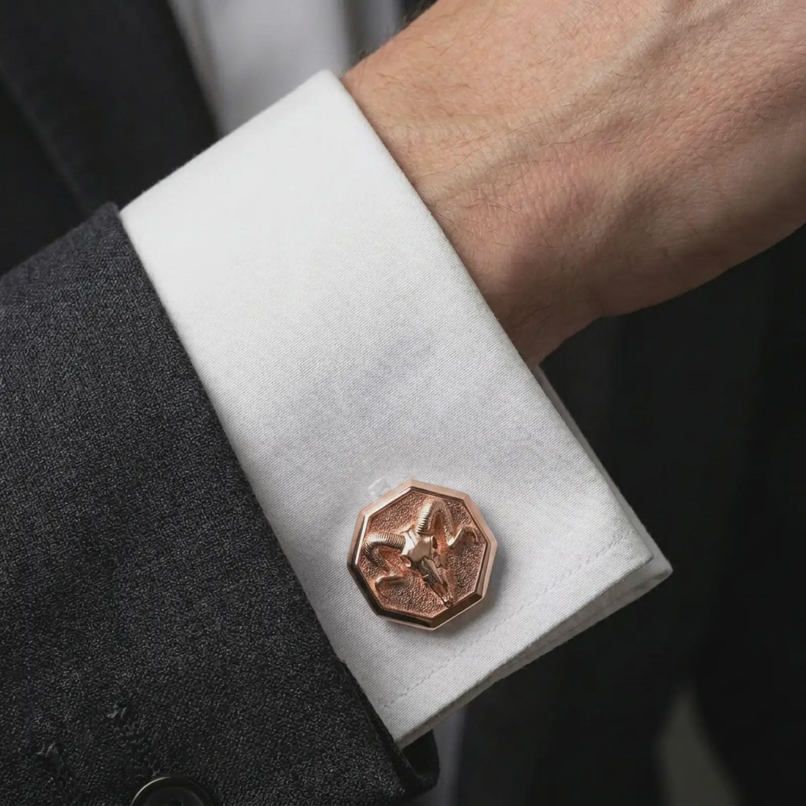 A rose gold plated ram skull cufflink is worn on a shirt cuff in a close-up lifestyle composition, highlighting its octagon frame and horned skull design.