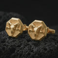Load image into Gallery viewer, Gold plated ram skull cufflinks sit on textured volcanic rock in a dramatic studio macro shot, highlighting the Aries-inspired skull motif and formal accessory design.
