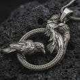 Load image into Gallery viewer, Oxidized Hugin and Munin ravens pendant necklace on textured volcanic rock, close-up studio shot highlighting Odin’s two ravens, braided circular frame, feather details, and antique silver contrast.

