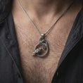 Load image into Gallery viewer, Oxidized Hugin and Munin ravens pendant necklace worn on the chest, close-up lifestyle jewelry photo showing the Norse Viking raven pendant on a spiga chain with dark clothing.

