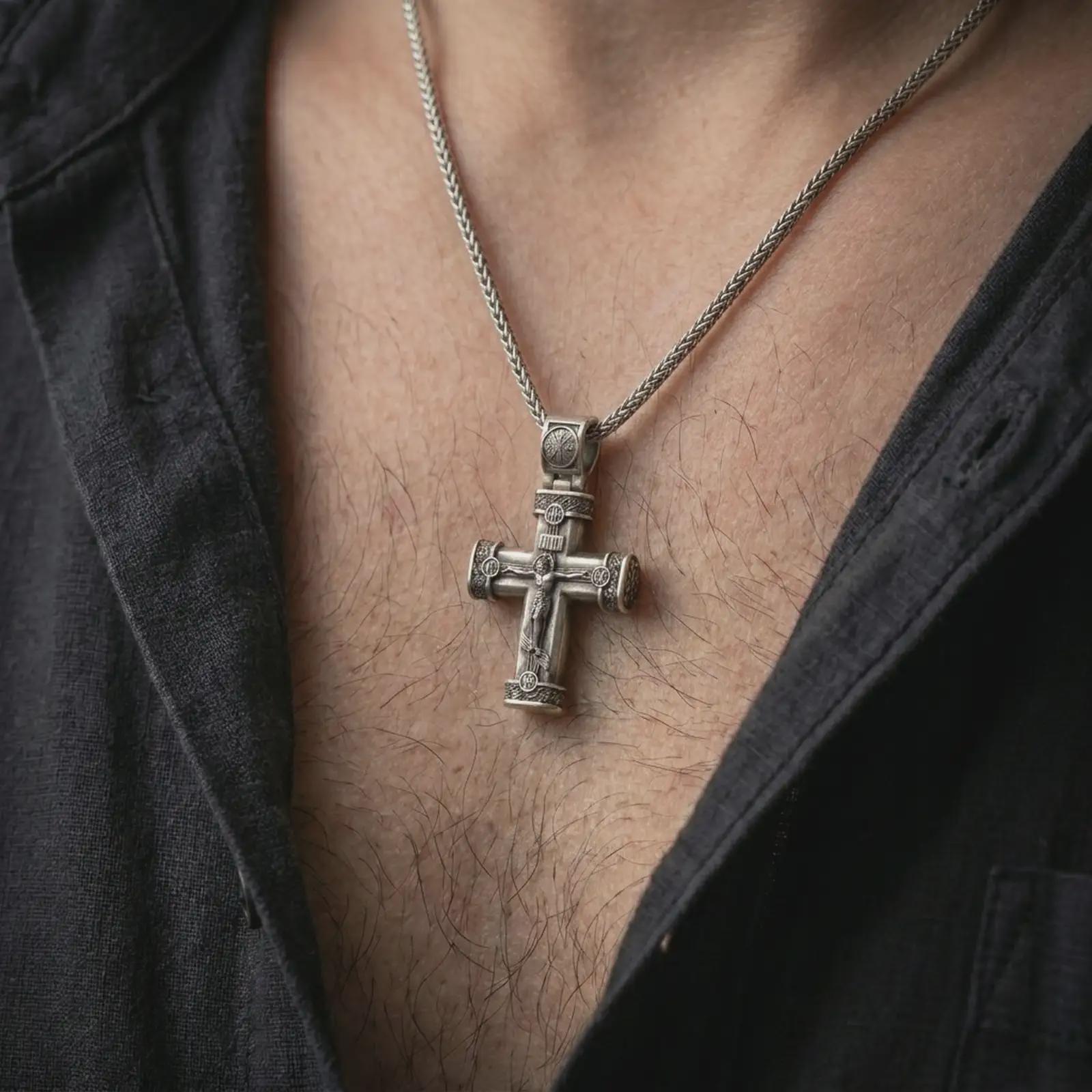 Oxidized crucifix cross pendant necklace worn on the chest, close-up lifestyle jewelry photo showing the Jesus cross on a spiga chain with dark clothing.