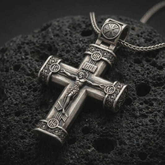 Oxidized crucifix cross pendant necklace on textured volcanic rock, close-up studio shot highlighting the Jesus figure, INRI plaque, ornate barrel ends, and antique silver contrast.