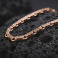 Load image into Gallery viewer, Rose gold plated Greek key chain necklace is photographed on porous volcanic rock in a close-up studio composition with refined patterned links.
