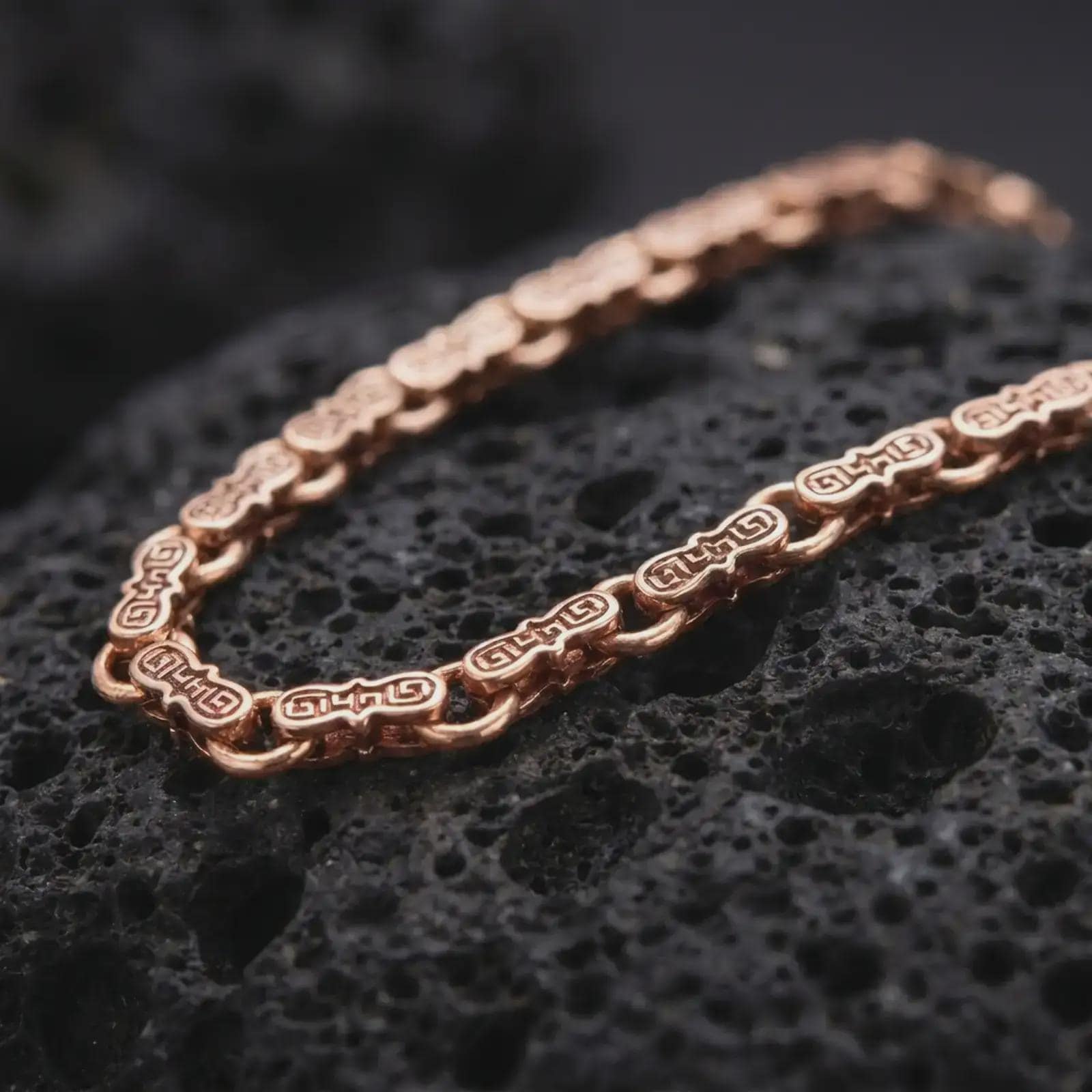 Rose gold plated Greek key chain necklace is photographed on porous volcanic rock in a close-up studio composition with refined patterned links.