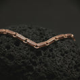 Load image into Gallery viewer, Rose gold plated Greek key chain photographed on black volcanic rock, showing its decorative patterned links and ancient Greek inspired design.
