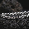 Load image into Gallery viewer, Polished silver ornamental chain necklace on volcanic stone, highlighting the sculpted link structure and bright reflective edges.
