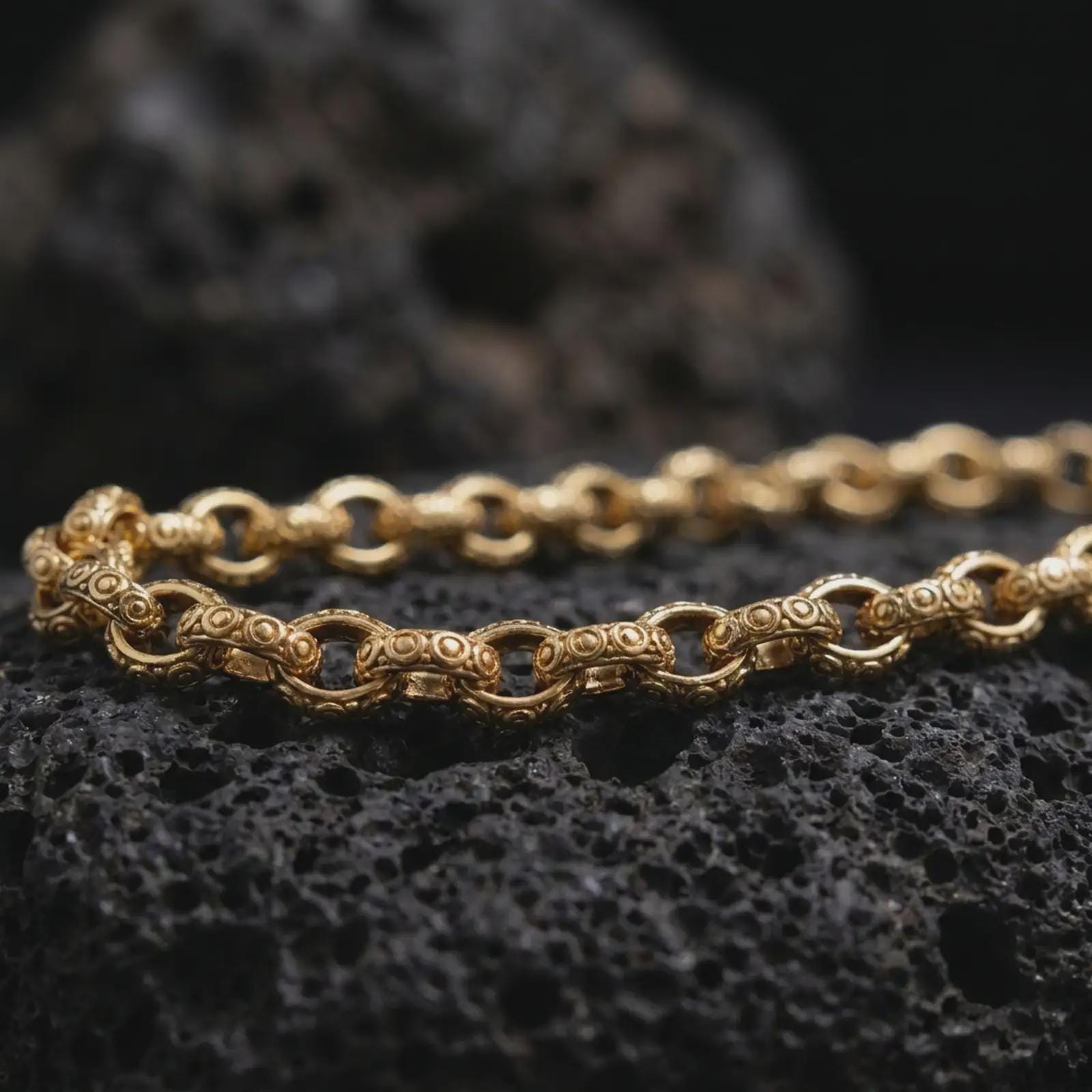 Gold plated ornamental link chain arranged across black rock, emphasizing the repeating circle pattern and decorative handcrafted texture.