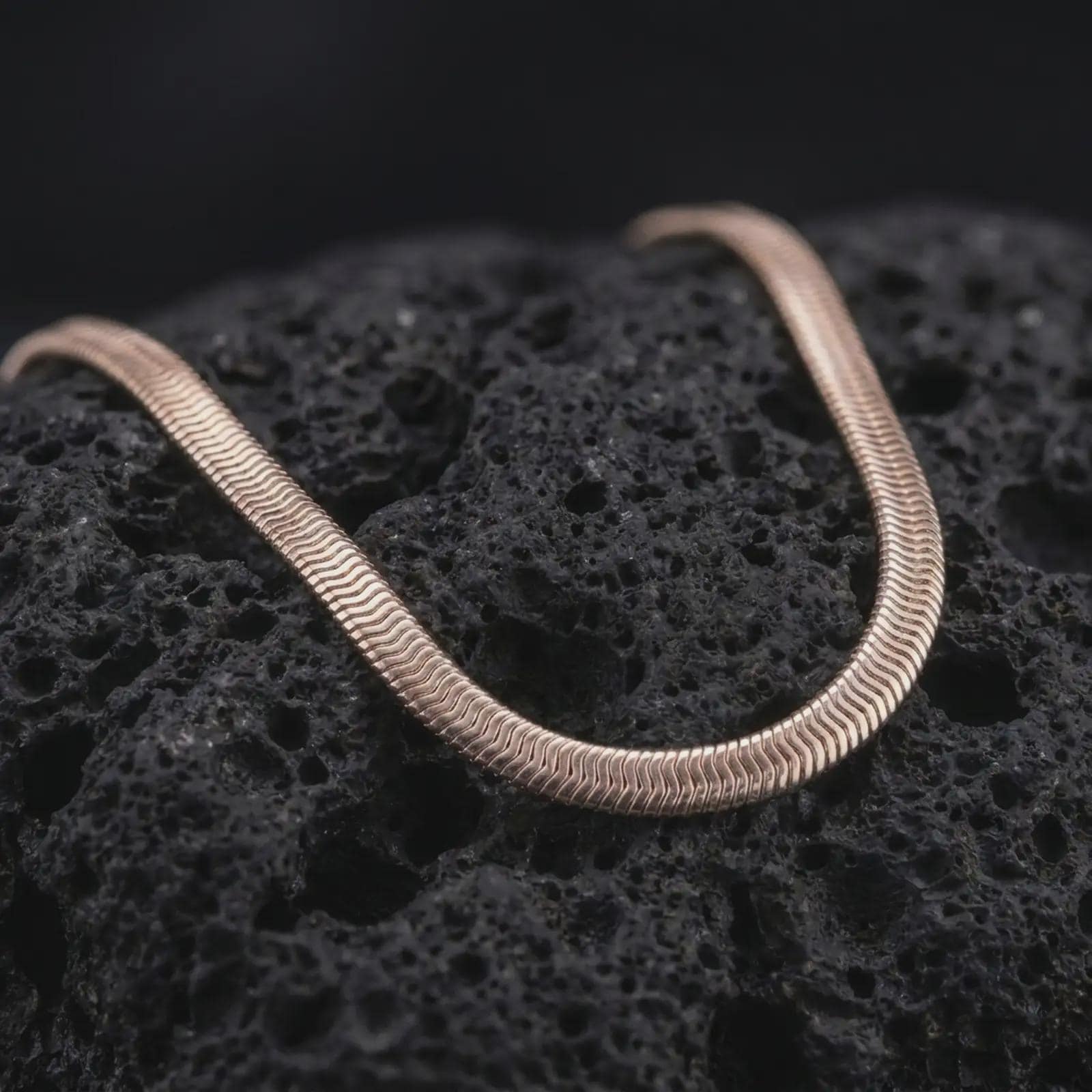 Rose gold plated snake chain necklace shown on dark volcanic stone, with a refined rounded silhouette and fluid link pattern.