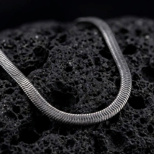 Oxidized sterling silver snake chain displayed on black volcanic rock, showing its smooth rounded profile and close flexible link structure.