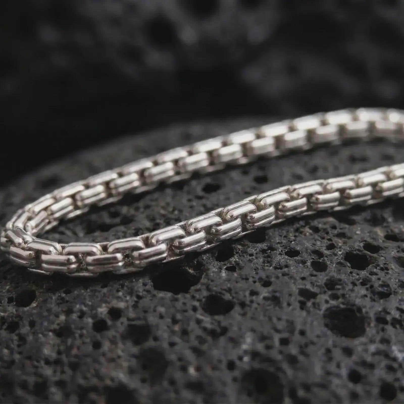 Polished silver box chain necklace on volcanic stone, highlighting the clean segmented link pattern and reflective sterling finish.