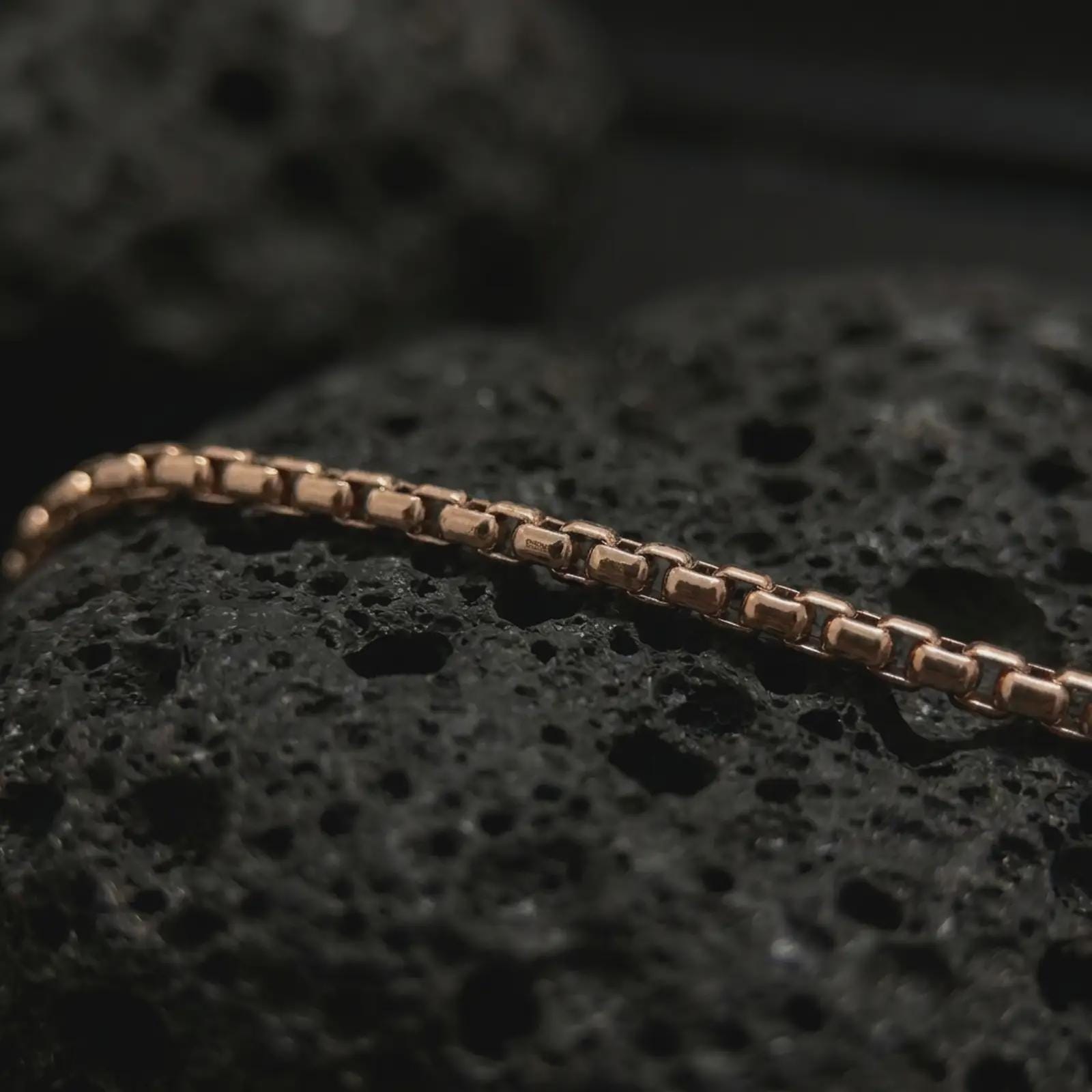Rose gold plated box chain necklace on dark volcanic stone, showing warm tone contrast with the precise square-link construction.