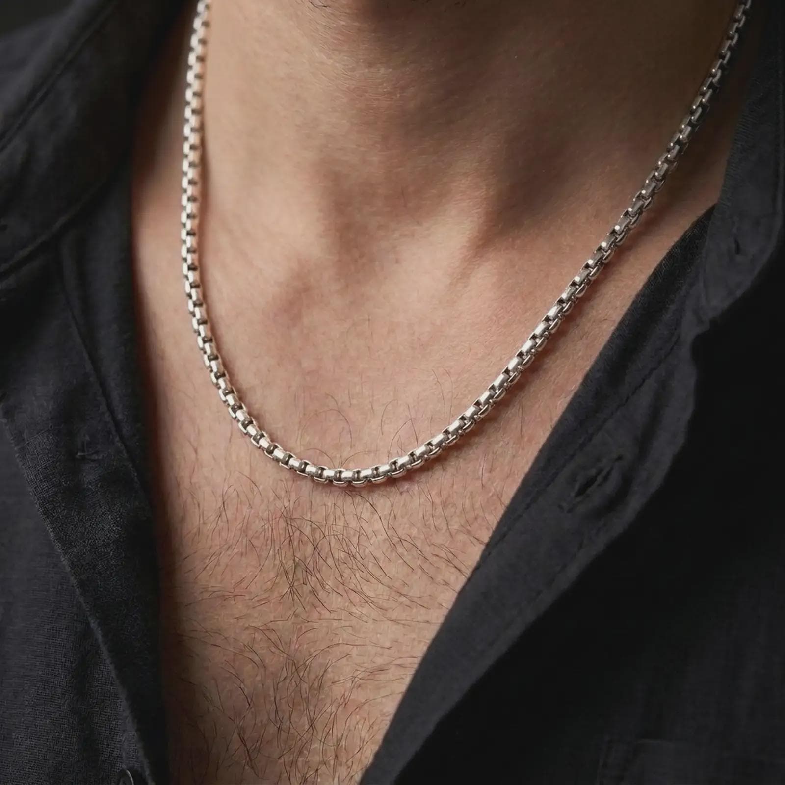 Oxidized silver box chain worn on a male model, styled as a sharp minimal necklace with a strong masculine profile.