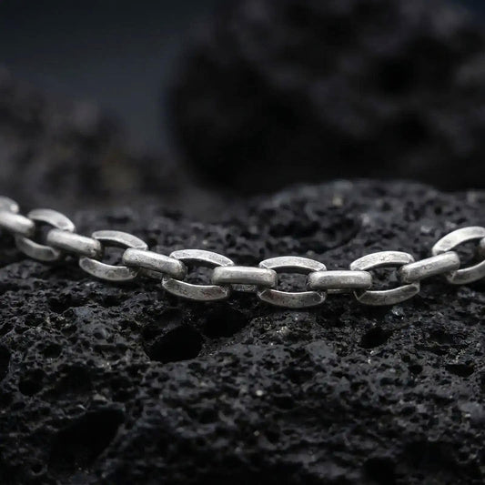 Oxidized sterling silver anchor link chain displayed on black volcanic rock, showing its rugged oval link construction.