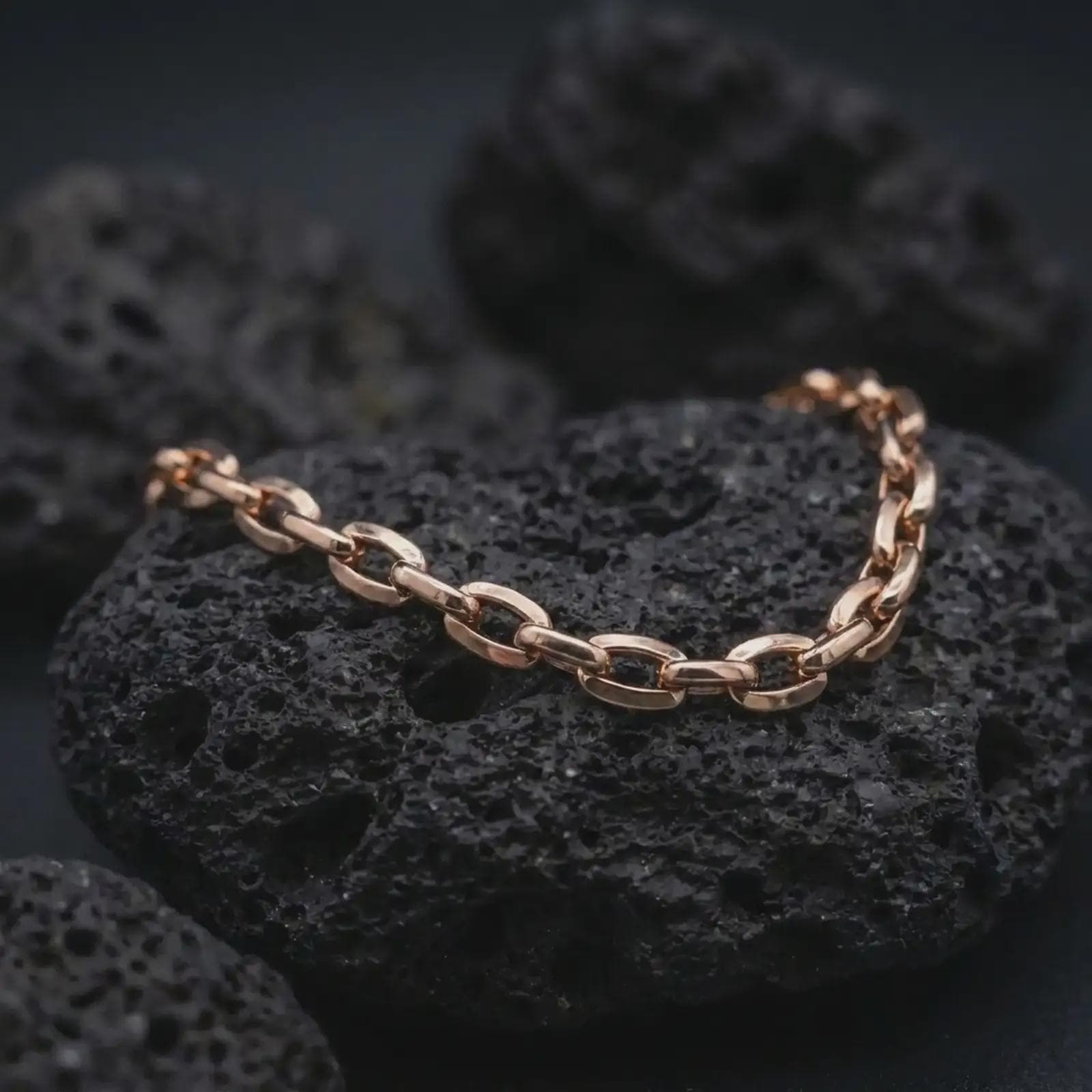 Rose gold plated anchor link bracelet on volcanic rock, showing a warm finish over a rugged men’s chain design.