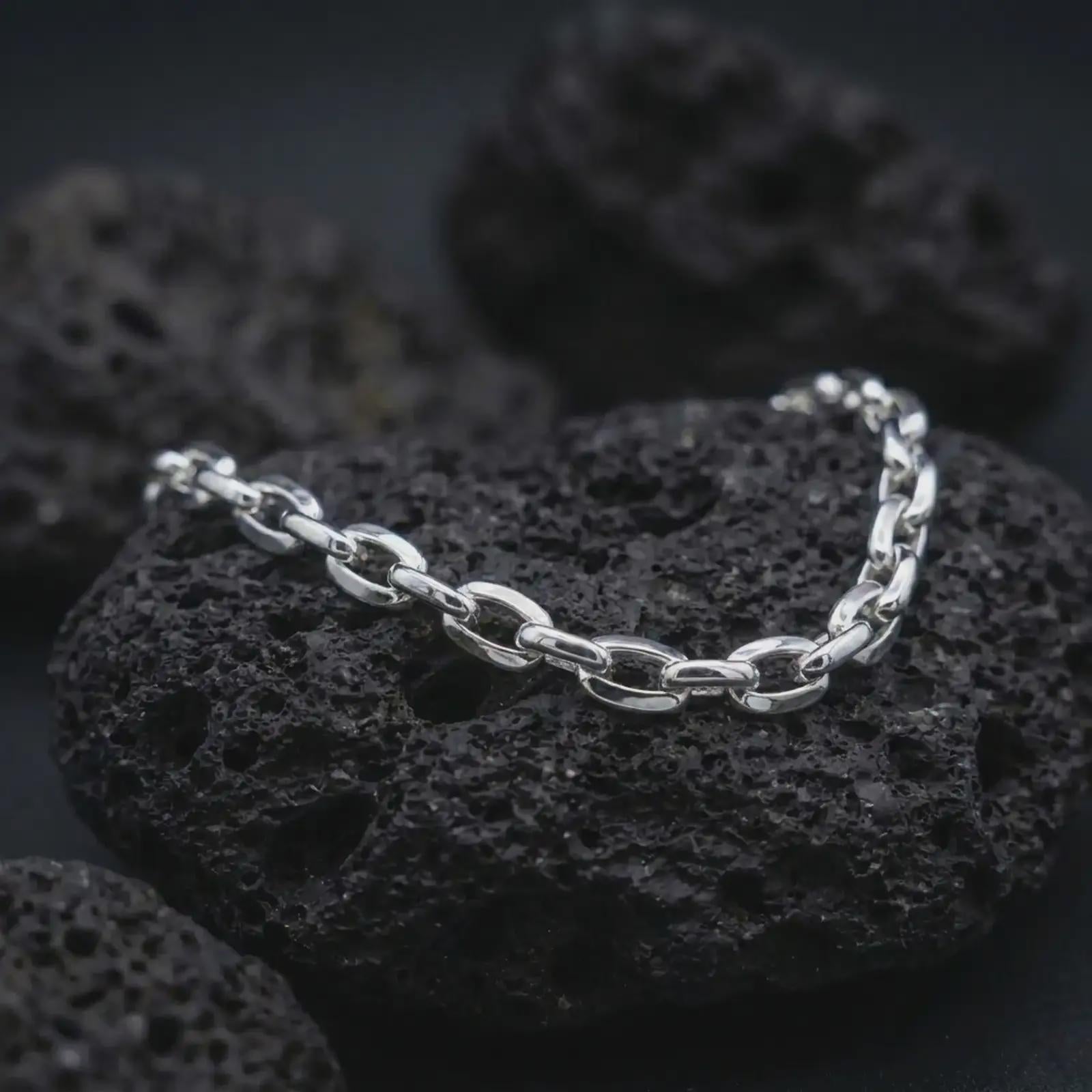 Polished silver anchor chain bracelet displayed on dark volcanic stone, emphasizing the clean oval link structure.