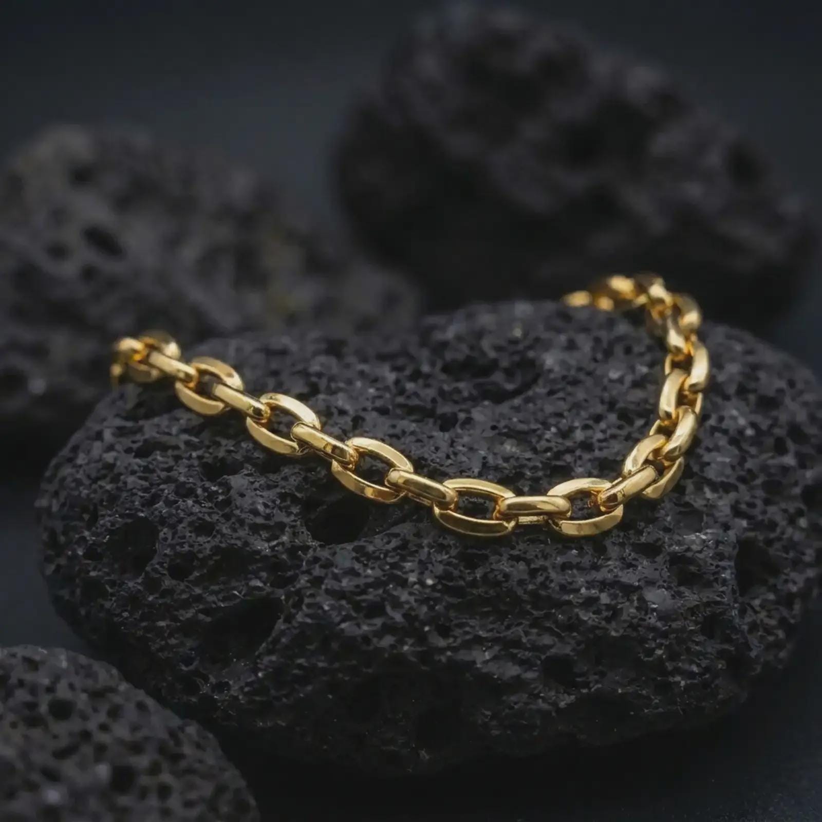 Gold plated mariner link bracelet resting on black lava rock, designed with bold nautical-inspired chain links.