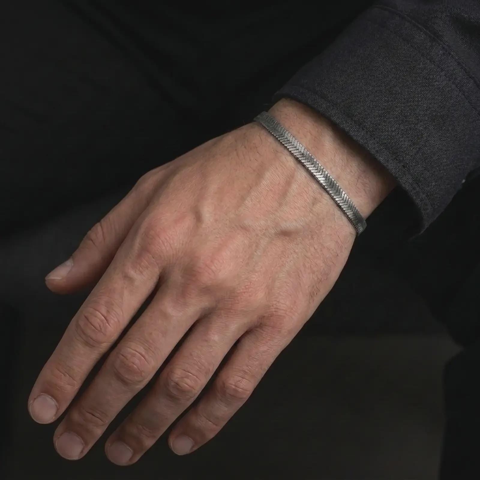 Oxidized silver herringbone bracelet worn on a male wrist, styled as a slim everyday bracelet with a masculine textured finish.