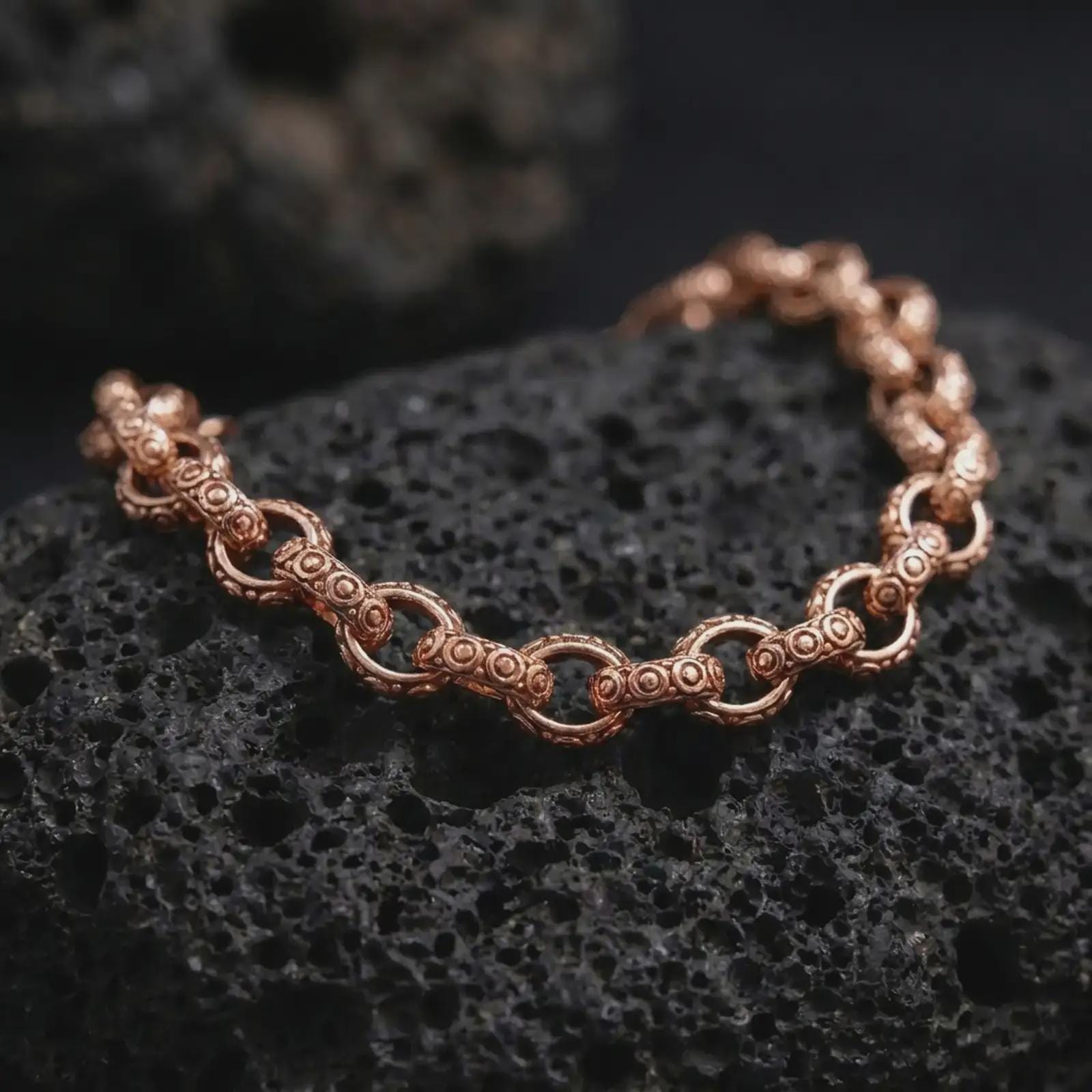 Rose gold plated vintage-style link bracelet displayed on volcanic stone, highlighting its open chain structure and decorative surface pattern.