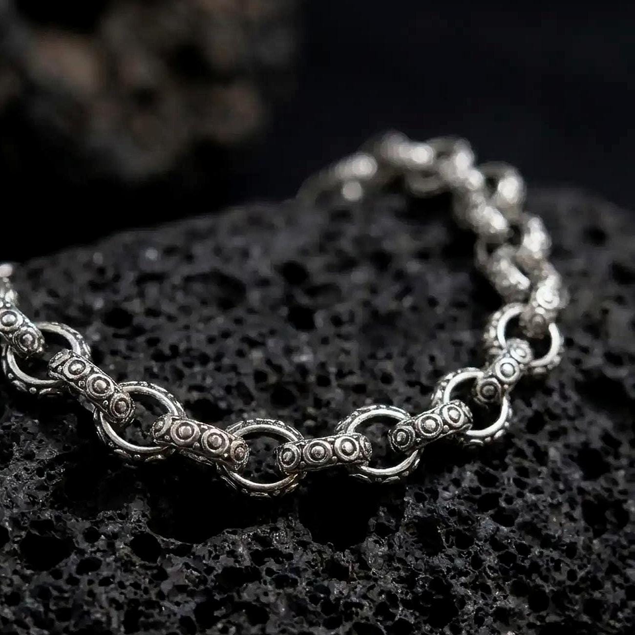 Oxidized sterling silver ornamental link bracelet displayed on black volcanic rock, showing raised circular details and vintage chain texture.