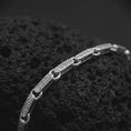 Load image into Gallery viewer, Greek meander chain bracelet in polished silver resting on textured volcanic rock in a detailed macro studio close-up.
