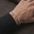 Load image into Gallery viewer, Polished silver Greek meander bracelet worn on a man’s wrist with the detailed chain links clearly visible in a lifestyle close-up.
