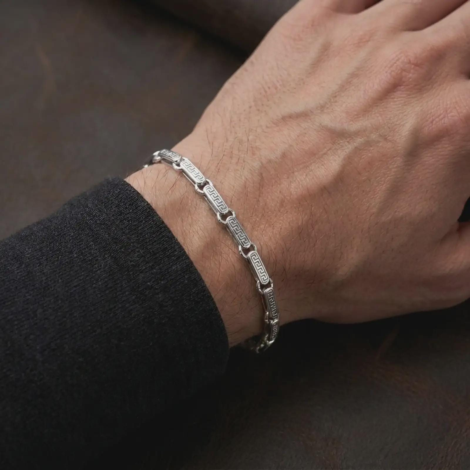 Polished silver Greek meander bracelet worn on a man’s wrist with the detailed chain links clearly visible in a lifestyle close-up.