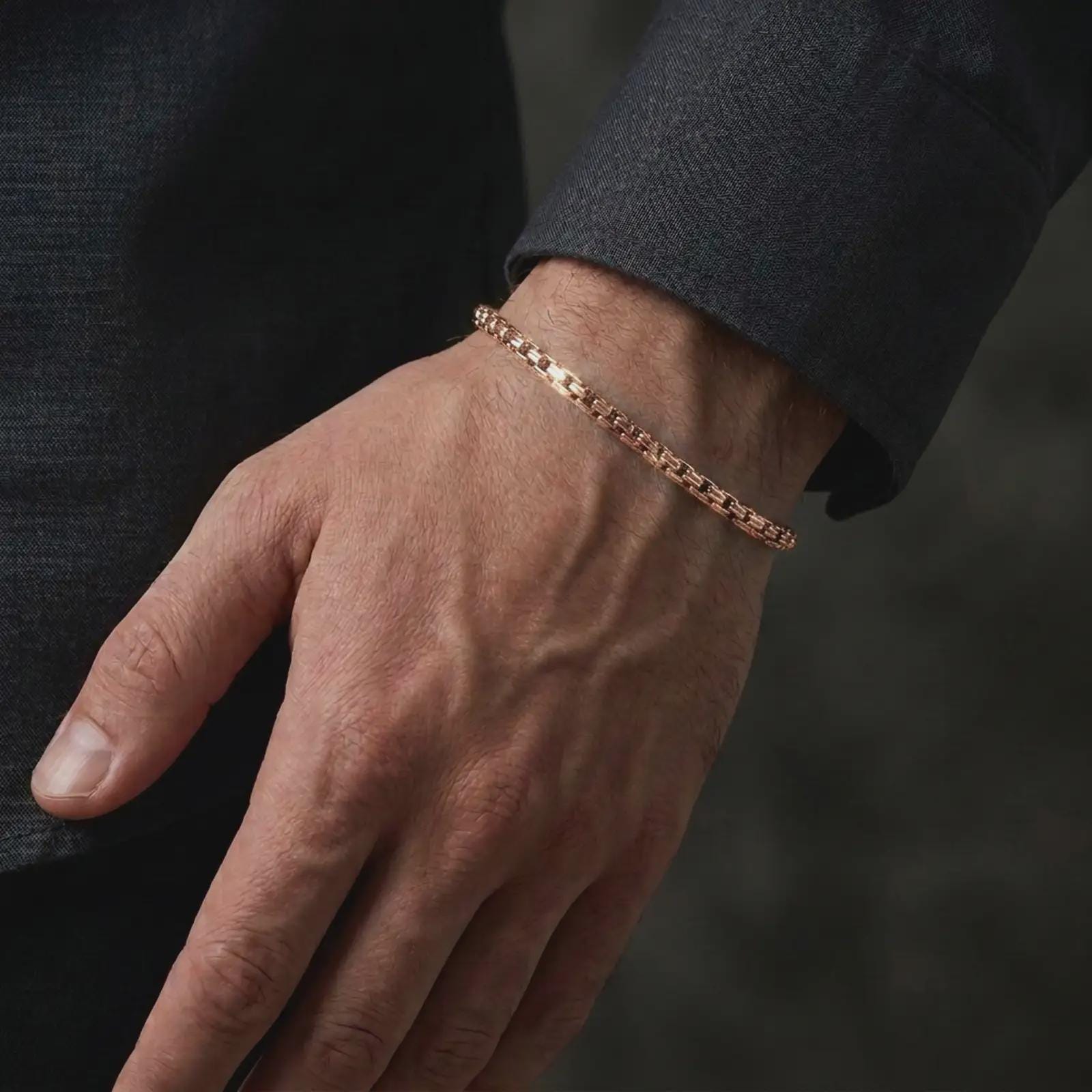 Rose gold plated men’s box chain bracelet worn on the wrist with a dark tailored sleeve, highlighting its minimalist profile and flexible geometric links in an elegant lifestyle close-up.