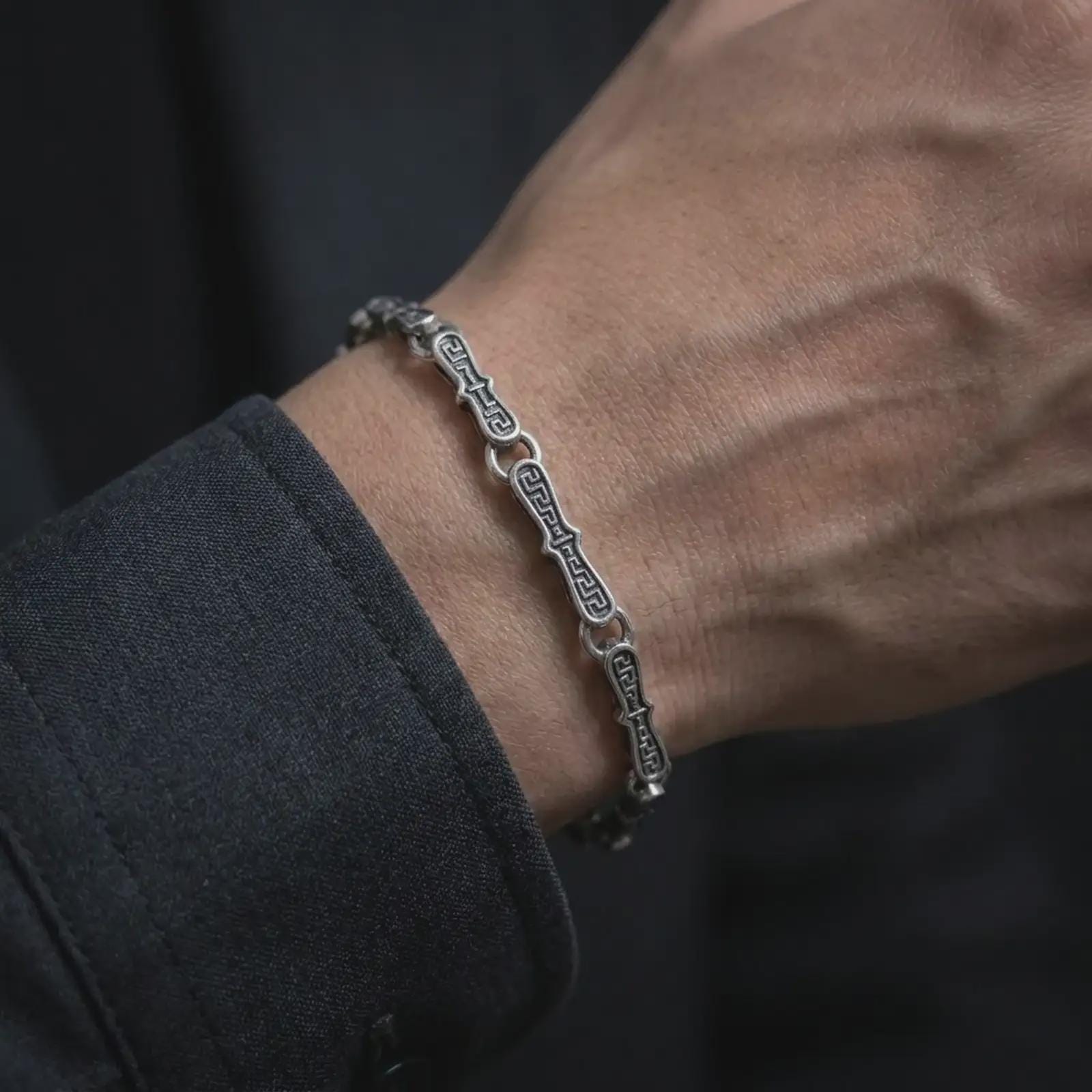 Oxidized Greek key bracelet worn on a man’s wrist, displaying the dark recessed meander engravings and elongated silver links in a masculine close-up lifestyle shot.