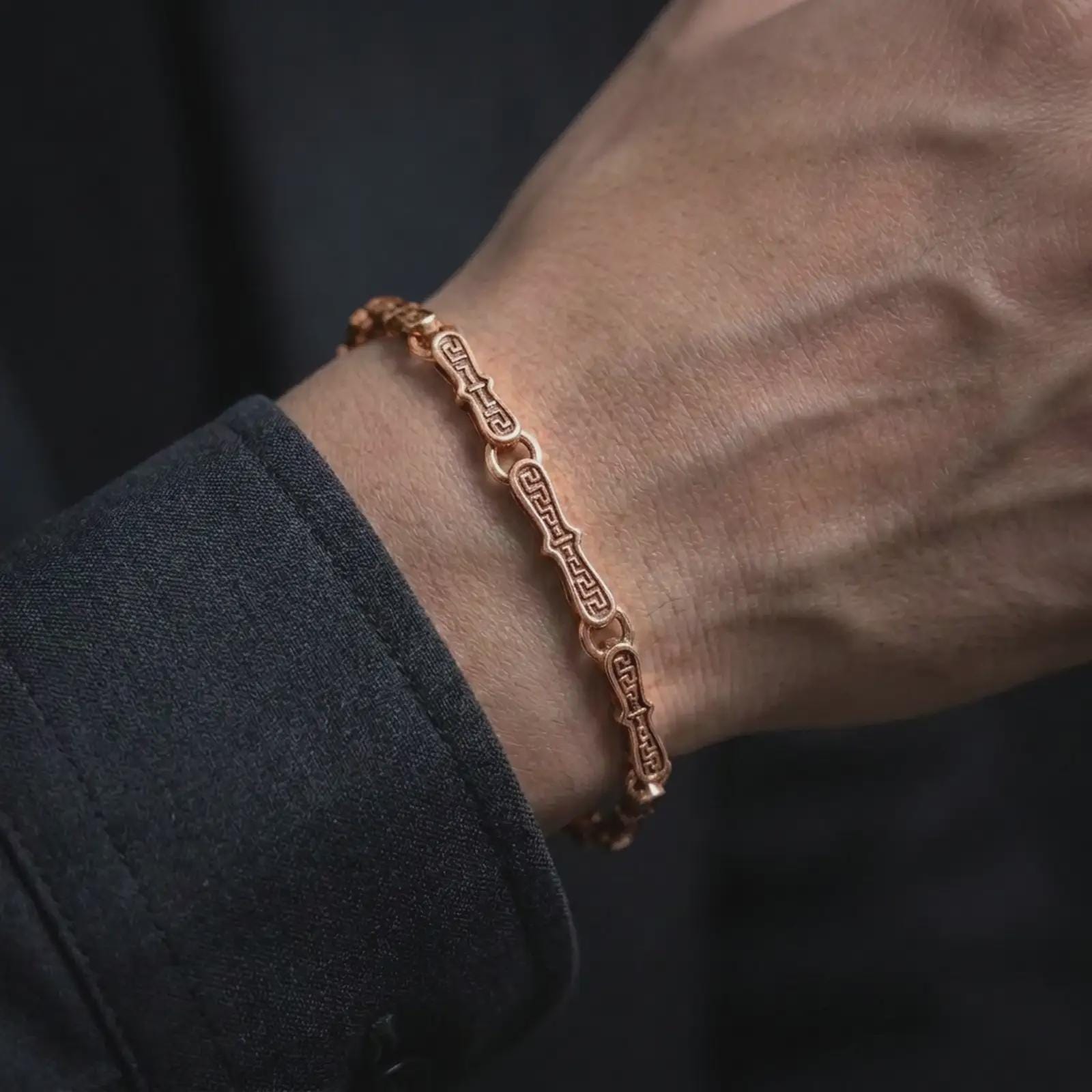 Rose gold plated Greek meander bracelet worn closely around a man’s wrist, featuring sculpted elongated links and repeating eternity details in an elegant lifestyle close-up.