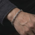 Load image into Gallery viewer, The polished silver Greek meander bracelet is worn closely around a man’s wrist, with the hourglass-shaped links and circular connectors clearly visible in a detailed lifestyle shot.

