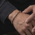 Load image into Gallery viewer, The rose gold plated Greek meander bracelet is worn on a man’s wrist, displaying its articulated bar-link structure and refined historical motif in an elegant lifestyle photograph.
