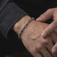 Load image into Gallery viewer, A Greek key bracelet with an oxidized finish is worn on a man’s wrist, showing the dark recessed pattern and linked sterling silver construction in a masculine lifestyle close-up.
