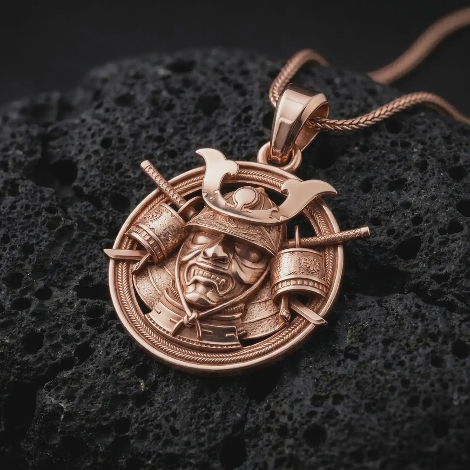 The rose gold plated Bushido warrior pendant is arranged on rugged black volcanic rock, emphasizing the detailed kabuto helmet, protective mask, shoulder armor, and braided border in a refined macro image.