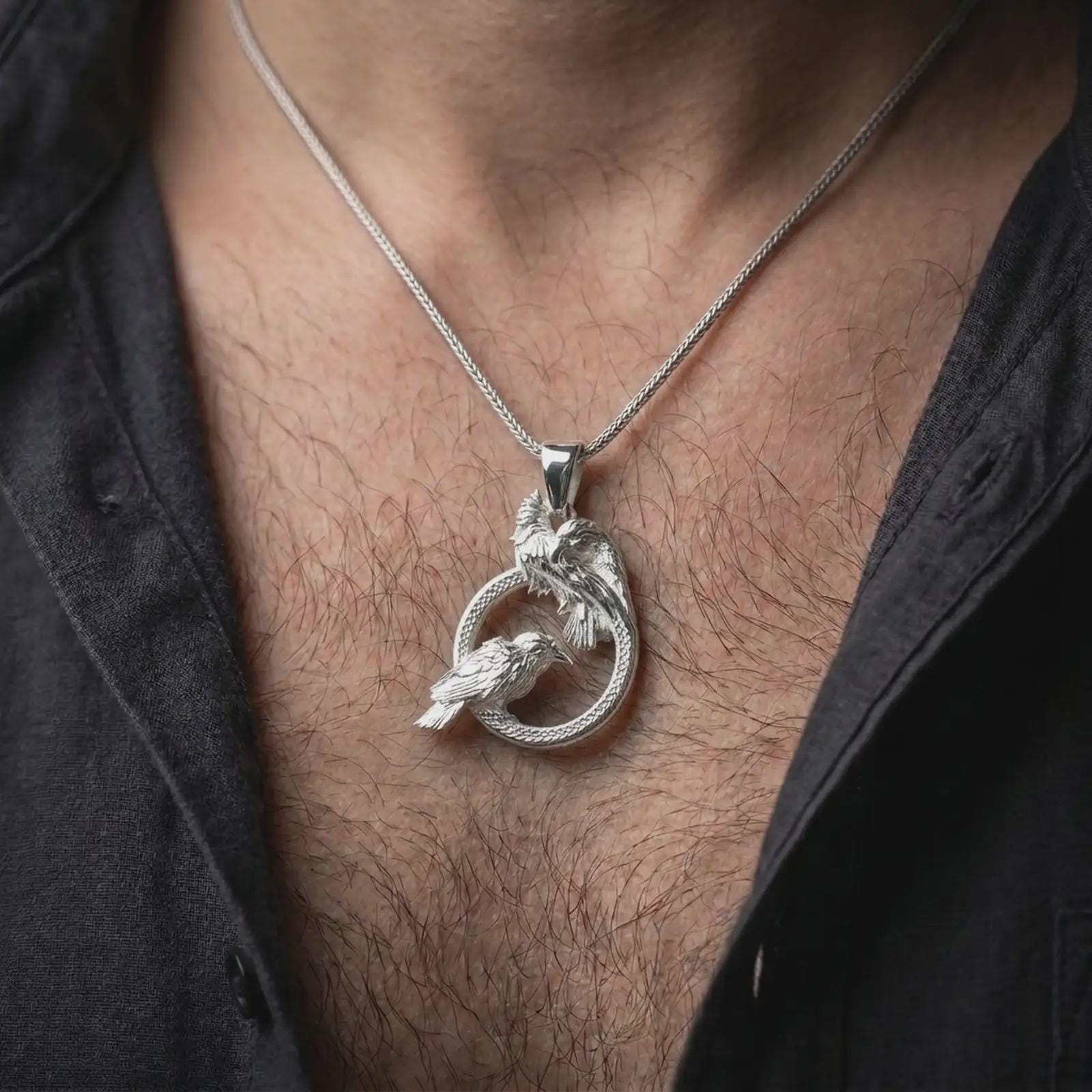 Polished silver Hugin and Munin ravens pendant necklace worn on the chest, masculine lifestyle shot highlighting the bright silver finish, sculpted feathers, and braided circular frame.