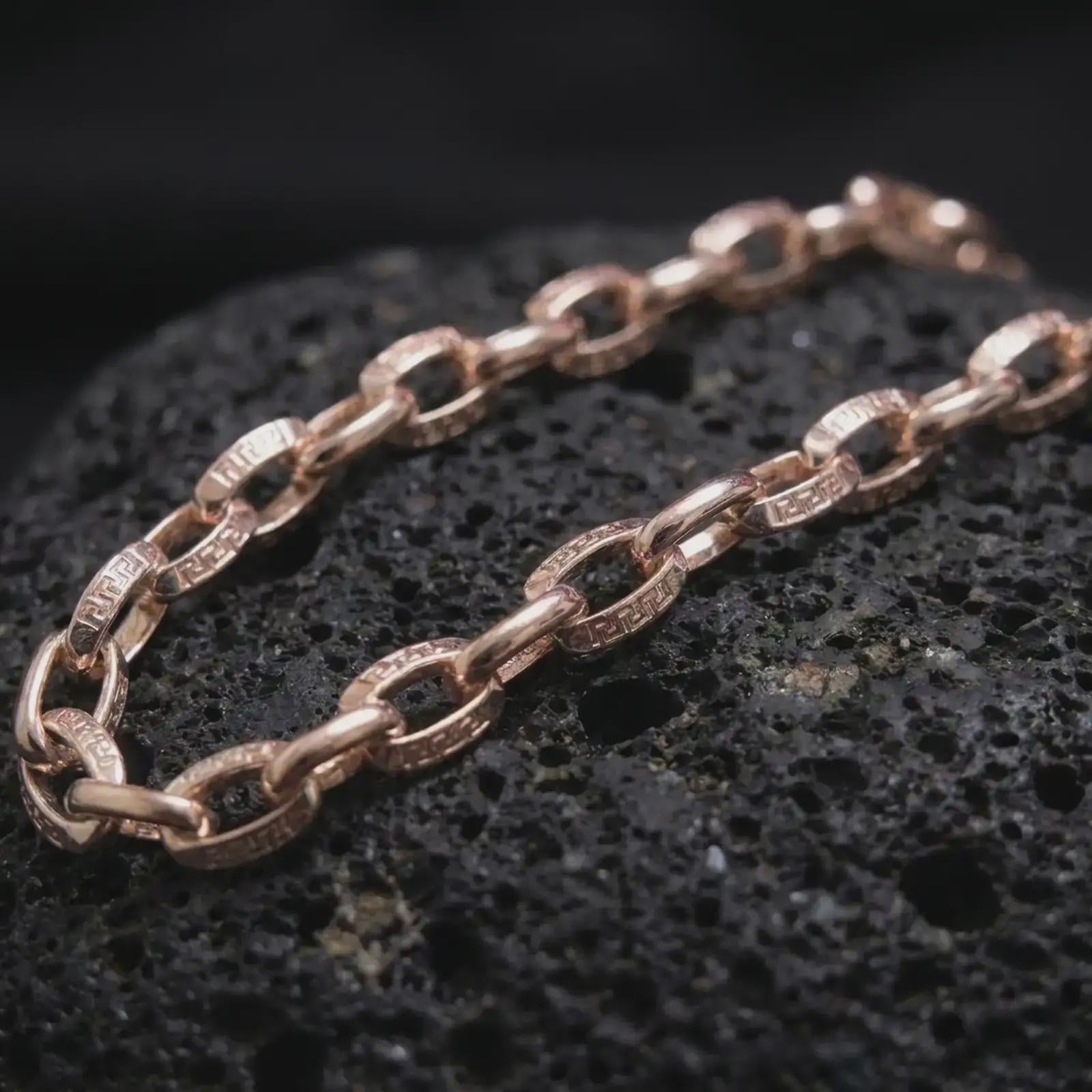 Rose gold plated Greek key chain necklace is photographed on porous volcanic rock in a close-up studio composition with refined luxury lighting and detailed links.