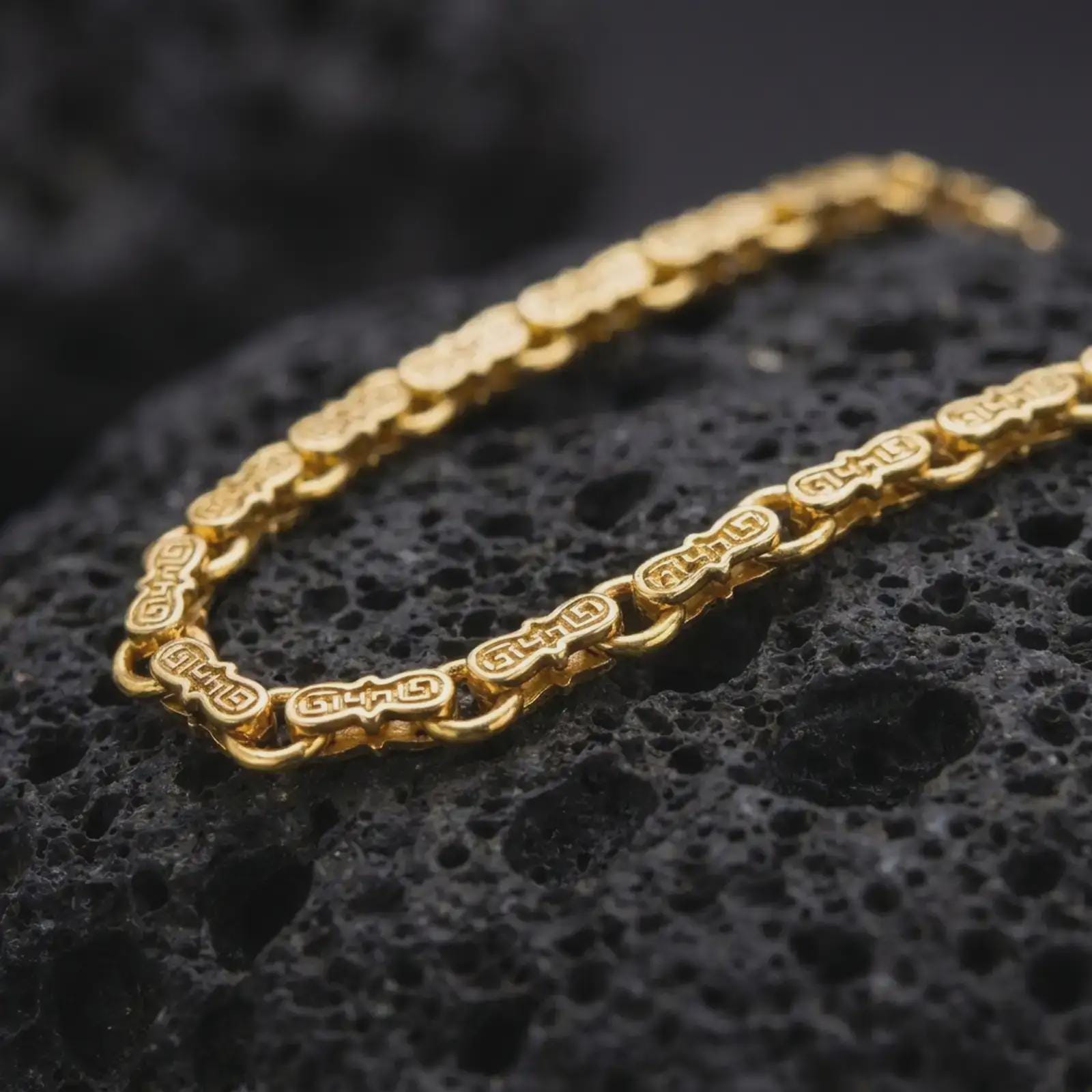 Gold plated Greek key chain necklace sits on textured volcanic rock in a dramatic studio macro shot, highlighting the repeating meander-style design.