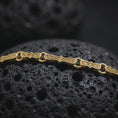 Load image into Gallery viewer, Gold plated Greek key chain necklace sits on textured volcanic rock in a dramatic studio macro shot, highlighting the repeating ancient Greek pattern.
