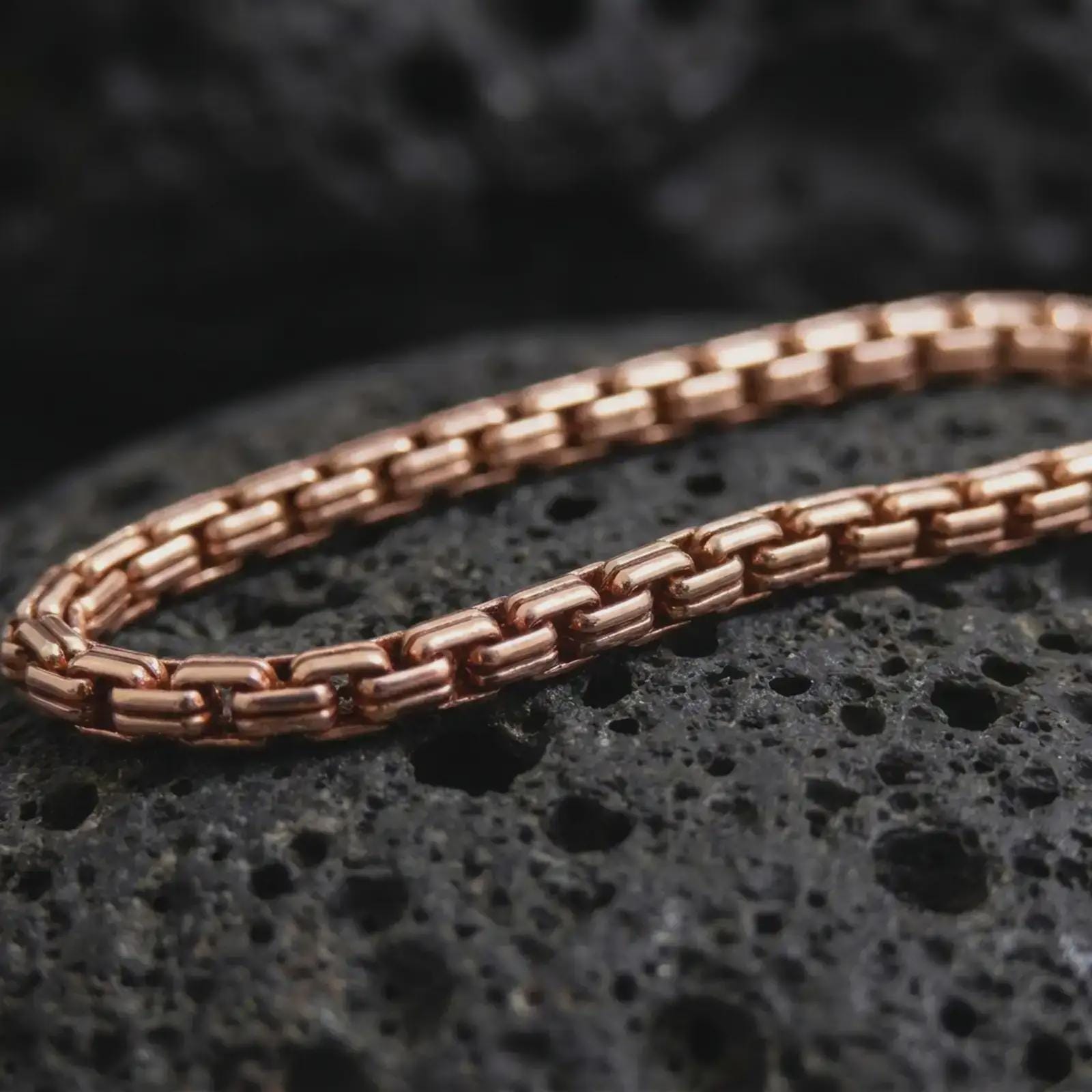 Rose gold plated box chain necklace shown on dark volcanic stone, with warm metal tone and defined rectangular link details.