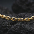 Load image into Gallery viewer, Gold plated anchor link chain arranged across dark volcanic rock, emphasizing its bold maritime chain structure.
