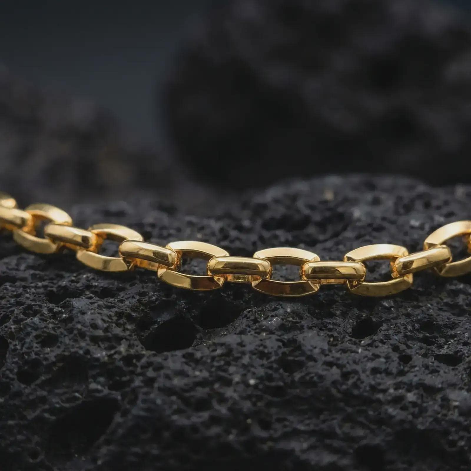 Gold plated anchor link chain arranged across dark volcanic rock, emphasizing its bold maritime chain structure.