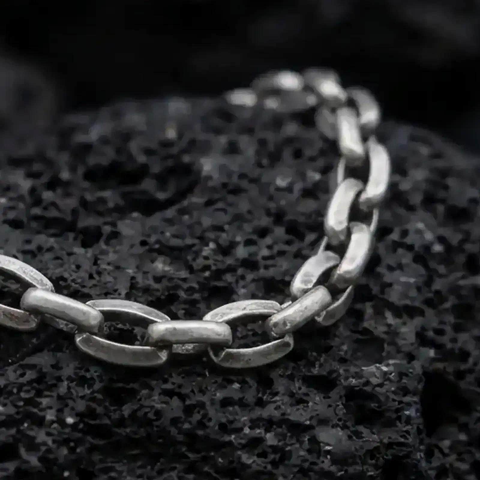 Oxidized sterling silver anchor link bracelet arranged on black volcanic rock, showing its rounded mariner-style links.